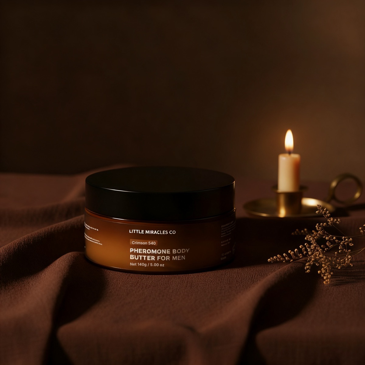 A jar of body butter on dark linen beside a lit candle